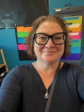 Image of teacher in front of a colorful classroom wall.